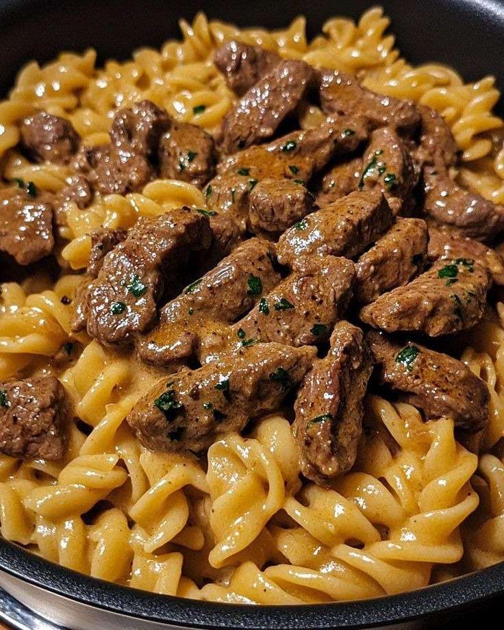 Creamy pasta tossed with seared steak strips in a garlic butter Parmesan cream sauce, finished with parsley and black pepper in a skillet