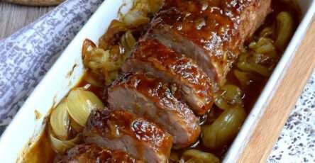 Roast pork with caramelized onions in a glossy honey sauce, sliced and served on a platter with golden cooking juices and tender onion wedges.