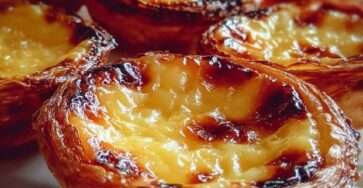 Golden Pastéis de Nata arranged on a plate, with flaky puff pastry shells and creamy custard centers caramelized on top, lightly dusted with cinnamon and powdered sugar.
