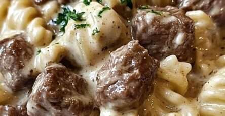 A bowl of Beef Rotini Pasta coated in creamy garlic Parmesan sauce with tender browned beef pieces, garnished with parsley and extra grated cheese.