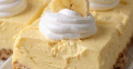 A no bake ultra creamy banana cheesecake with a golden biscuit crust, smooth banana filling, topped with whipped cream and fresh banana slices on a serving plate.