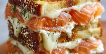 Golden smoked salmon and Boursin croque made with toasted white bread, melted cheese on top, creamy filling, and fresh dill, served hot on a plate.