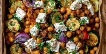 Sheet pan with roasted zucchini rounds, crispy chickpeas, red onion wedges, red bell pepper strips, and warm feta, finished with parsley and lemon