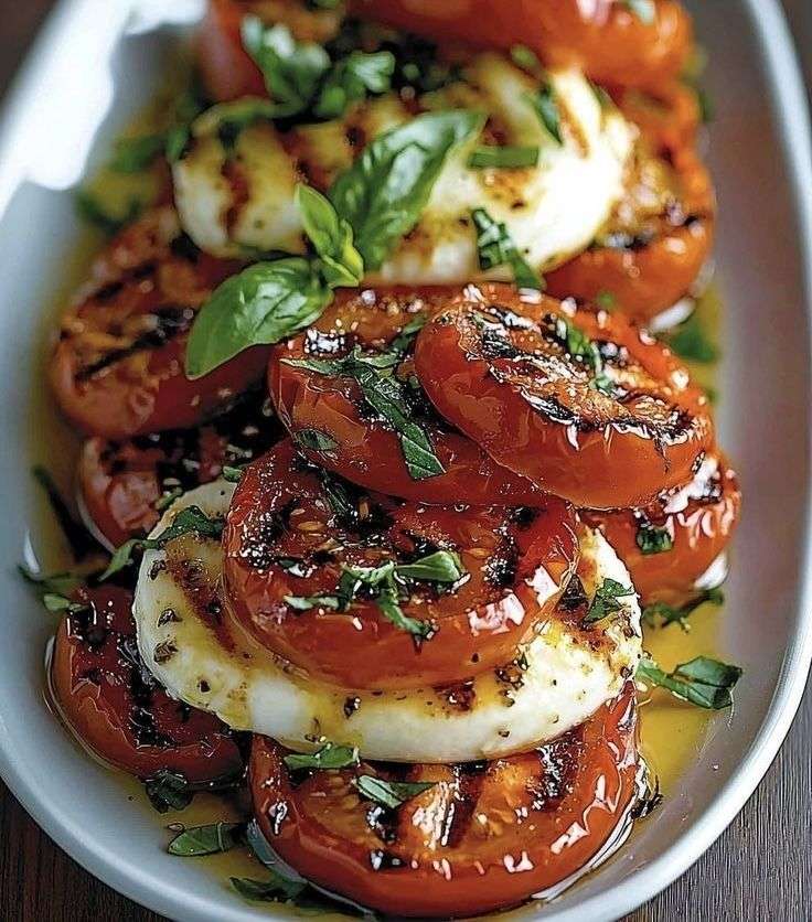 Roasted tomato halves layered with fresh mozzarella slices and basil leaves, drizzled with balsamic and olive oil, served on a platter