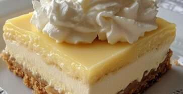 No-bake lemon cheesecake bars with a buttery biscuit crust, creamy cheesecake layer, glossy lemon curd topping, and whipped cream decoration on top.