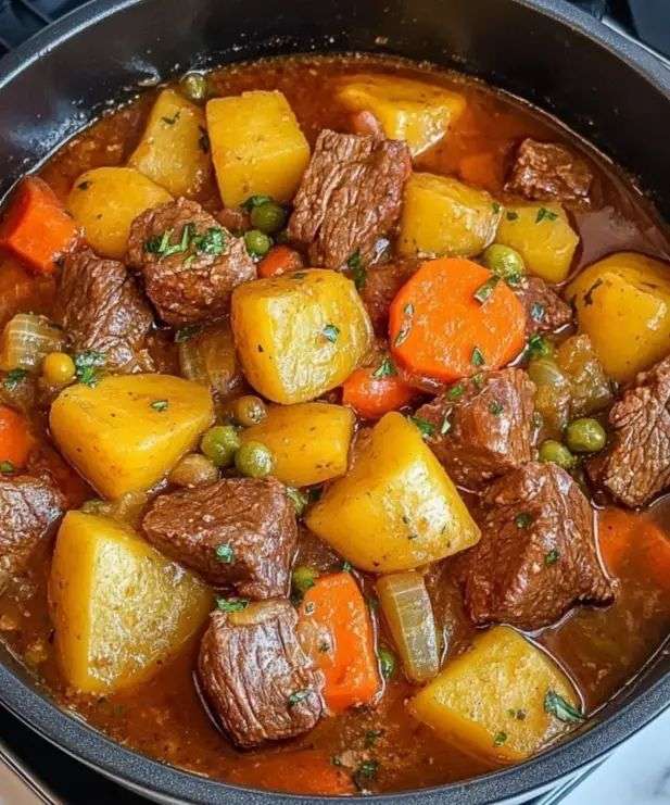 Hearty beef stew in a rustic bowl with tender beef chunks, soft potatoes, carrots, and peas in a rich thick broth garnished with fresh parsley.