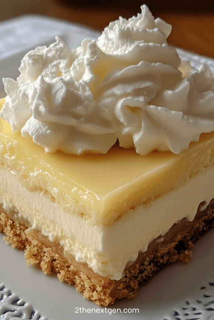No-bake lemon cheesecake bars with a buttery biscuit crust, creamy cheesecake layer, glossy lemon curd topping, and whipped cream decoration on top.