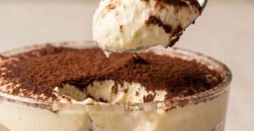 Classic Italian tiramisu recipe served in a glass dish with visible layers of espresso-soaked ladyfingers, creamy mascarpone filling, and cocoa powder on top