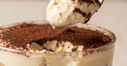 Classic Italian tiramisu recipe served in a glass dish with visible layers of espresso-soaked ladyfingers, creamy mascarpone filling, and cocoa powder on top