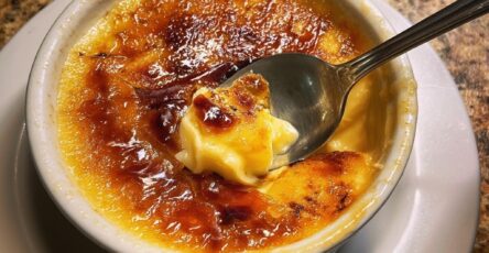 Classic vanilla crème brûlée in ceramic ramekins with a smooth creamy custard and a golden caramelized sugar crust, slightly cracked on top, served with a spoon.