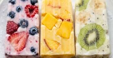 Yogurt fruit popsicles recipe with colorful frozen yogurt bars filled with fresh fruit pieces on a clean background