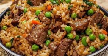 Beef fried rice in a wok with tender beef strips, fluffy rice grains, peas, carrots, and green onions, lightly coated in soy sauce and garnished fresh.