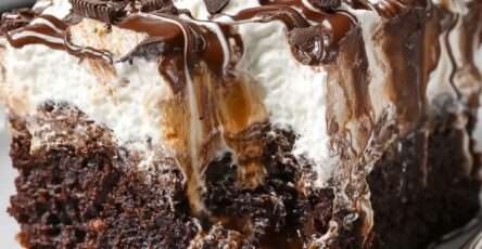 Chocolate caramel poke cake sliced into squares with whipped cream topping, caramel drizzle, chocolate sauce, and chocolate shavings.