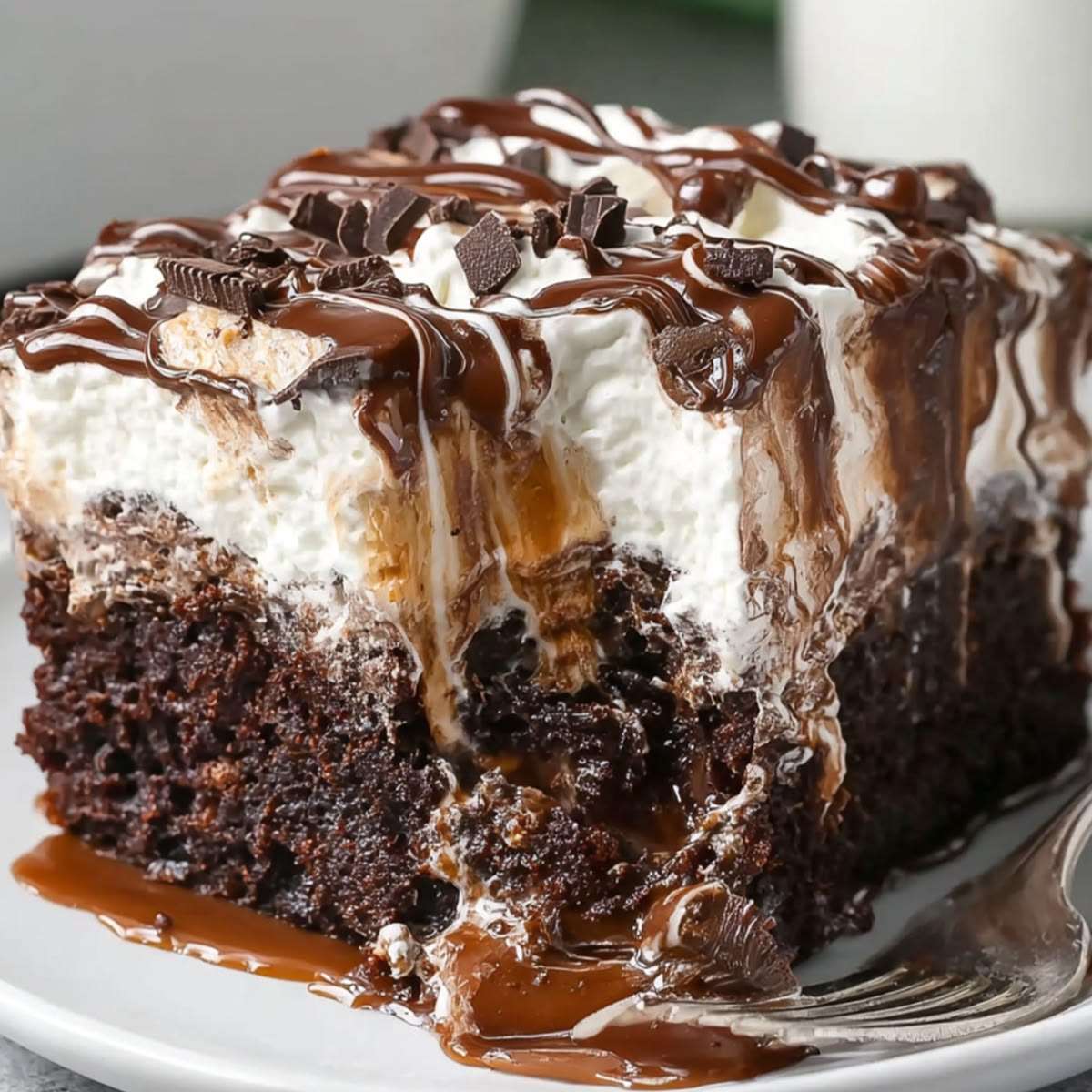 Chocolate caramel poke cake sliced into squares with whipped cream topping, caramel drizzle, chocolate sauce, and chocolate shavings.
