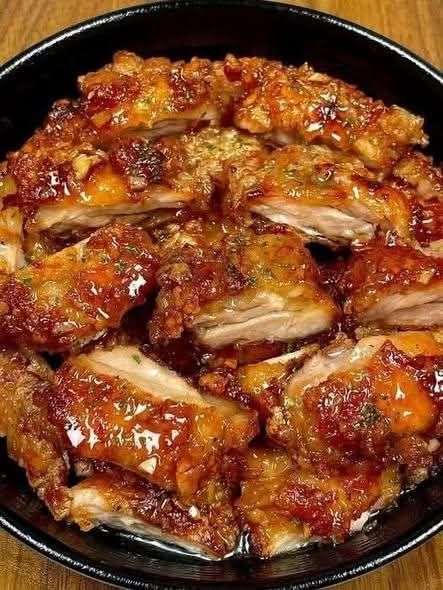 Crispy honey garlic chicken thighs sliced and served with sticky glaze, sesame seeds, green onions, and extra sauce on top.