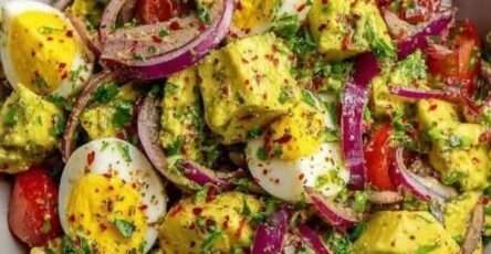 A clear glass bowl filled with a colorful avocado and egg salad, showcasing hard-boiled egg quarters, diced green avocado, red onion slices, and cherry tomatoes.