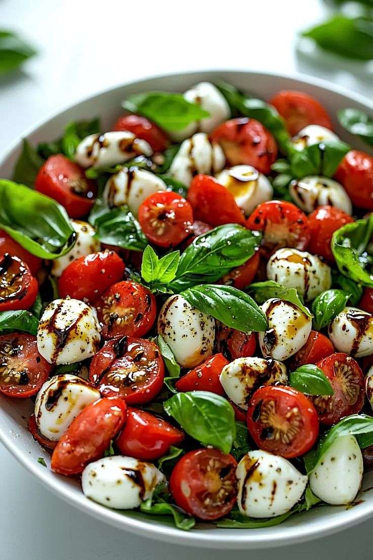 Fresh Caprese salad served in a bowl with halved cherry tomatoes, creamy mini mozzarella balls, bright basil leaves, olive oil, and balsamic glaze.
