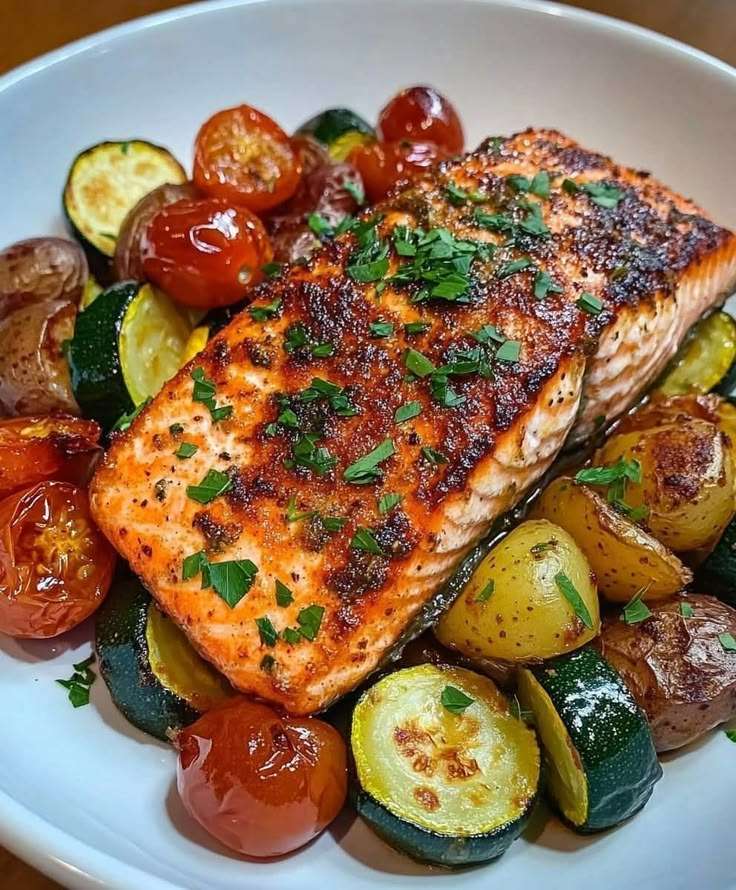 Garlic herb salmon fillets baked over roasted baby potatoes, zucchini, cherry tomatoes, lemon, garlic, parsley, and herbs.