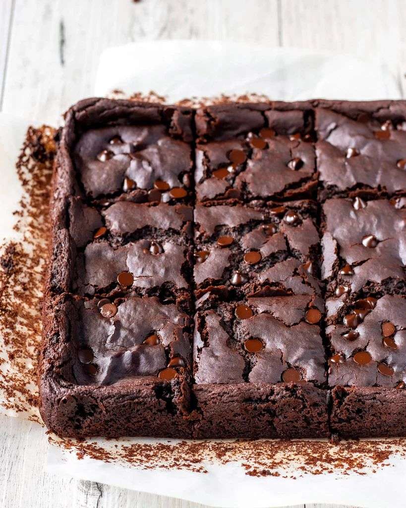 Fudgy chocolate chip brownies sliced into squares with a shiny crackly top, melted chocolate chips, and a rich soft chocolate center.