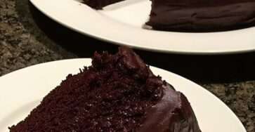 Ultra-moist chocolate cake covered with glossy chocolate ganache, sliced on a plate with a soft rich crumb and shiny topping.