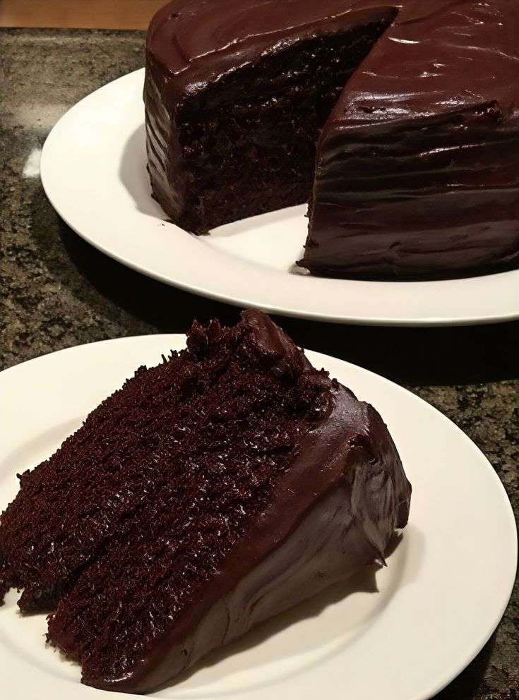 Ultra-moist chocolate cake covered with glossy chocolate ganache, sliced on a plate with a soft rich crumb and shiny topping.