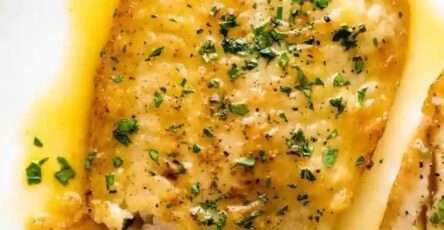 Lemon butter fish fillets served with glossy garlic lemon butter sauce, fresh parsley, lemon wedges, and a side of vegetables.