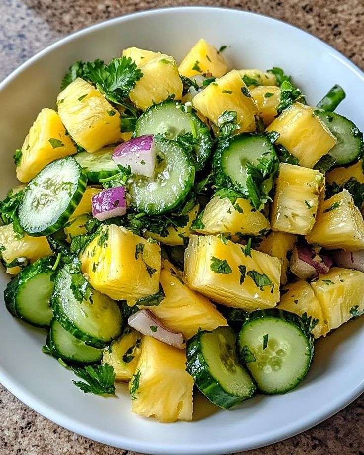 Fresh pineapple cucumber salad with juicy pineapple cubes, cucumber slices, red onion, herbs, lime dressing, and chili flakes in a bowl.