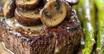 Seared steak served with creamy mushroom sauce, sautéed asparagus, fresh thyme, garlic butter, and cracked black pepper on a plate.