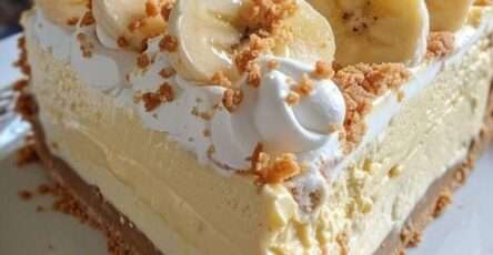 No-bake banana cream cheesecake with buttery biscuit crust, creamy banana filling, whipped cream, banana slices, crushed biscuits, and caramel drizzle.