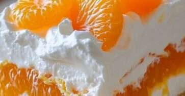 A rectangular glass baking dish displaying a layered dessert with a golden graham cracker crust, a thick white cream layer, and bright orange mandarin slices arranged on top.