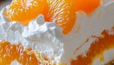 A rectangular glass baking dish displaying a layered dessert with a golden graham cracker crust, a thick white cream layer, and bright orange mandarin slices arranged on top.