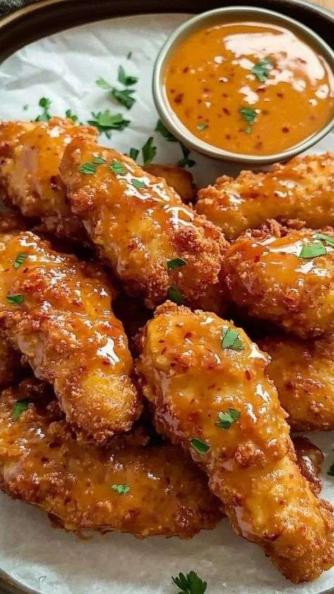 A platter of golden brown crispy chicken tenders covered in a shiny red sweet chili glaze and topped with finely chopped fresh green herbs.