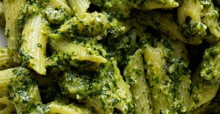 Creamy pesto penne pasta served in a bowl with green basil sauce, grated parmesan, black pepper, fresh basil leaves, and a rich creamy texture.