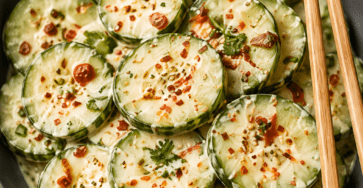 Close-up of viral cucumber salad with thin cucumber slices tossed in creamy chili garlic dressing, topped with sesame seeds, herbs, and red chili flakes.