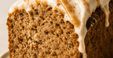 Close-up of banana bread latte cake slice with moist banana crumb, cinnamon coffee glaze, caramel drizzle, chopped walnuts, and a warm coffee cup in the background.