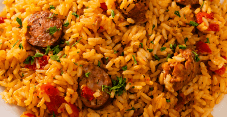 A hearty sausage chicken rice skillet served hot with fluffy yellow rice, browned chicken pieces, smoked sausage slices, red bell pepper, parsley, and lemon wedges.