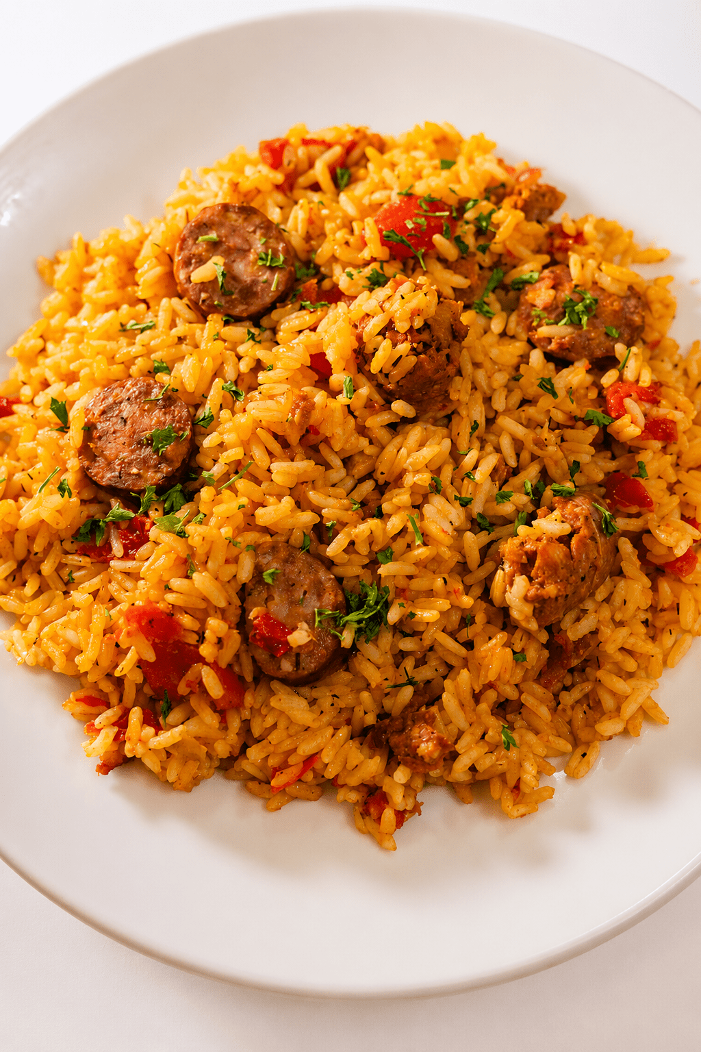 A hearty sausage chicken rice skillet served hot with fluffy yellow rice, browned chicken pieces, smoked sausage slices, red bell pepper, parsley, and lemon wedges.