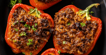 Baked stuffed red bell peppers filled with seasoned ground beef, rice, tomato sauce, herbs, and melted cheese, served hot with fresh parsley on top.