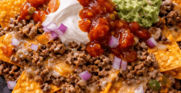 Loaded beef nachos served on a tray with crispy tortilla chips, seasoned ground beef, melted cheddar, guacamole, salsa, sour cream, red onion, jalapeños, and fresh cilantro.