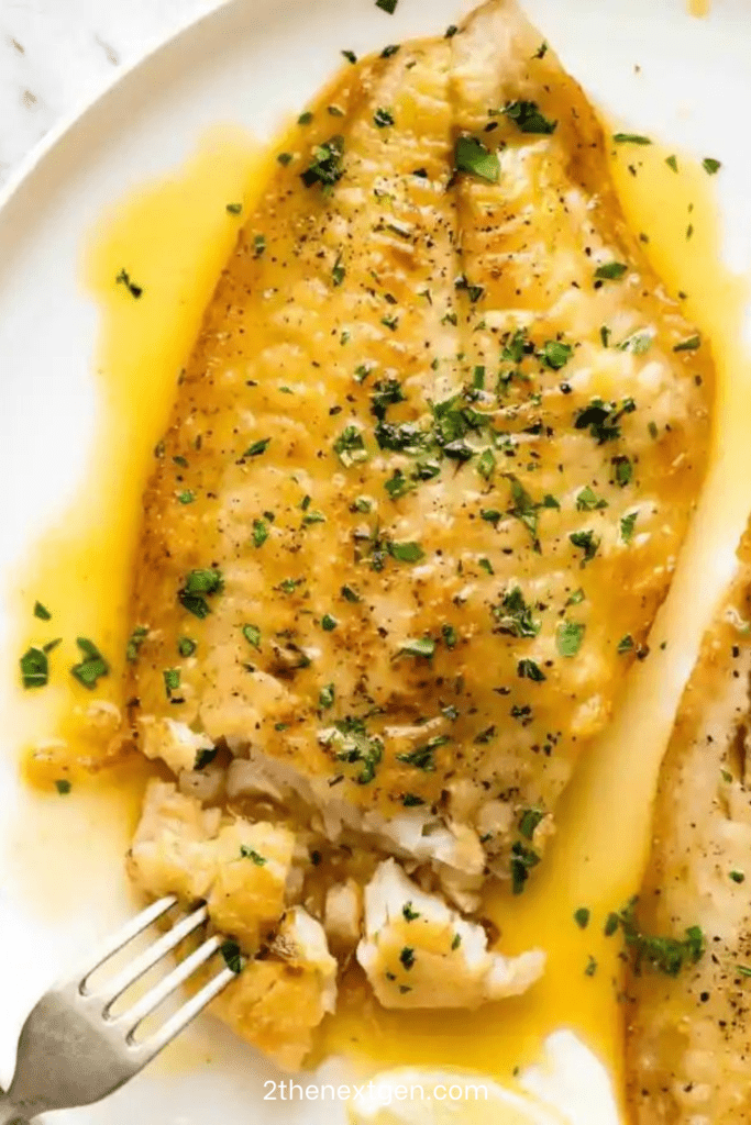 Lemon butter fish fillets served with glossy garlic lemon butter sauce, fresh parsley, lemon wedges, and a side of vegetables.