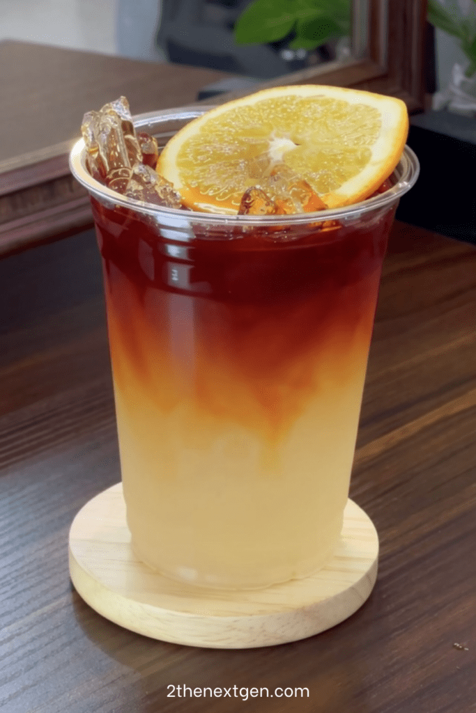 Iced lemon tea lemonade served in tall glasses with fresh lemon slices, orange slices, ice cubes, black tea layer, and mint leaves.