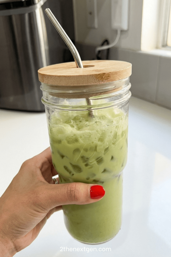 A tall mason jar filled with creamy iced matcha latte made with oat milk and nugget ice. The vibrant green matcha layer swirls beautifully through the milk, creating a marbled effect. The drink is served with a metal straw and lid, making it a refreshing and aesthetic homemade beverage.