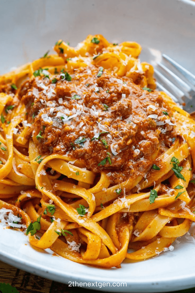Tagliatelle Bolognese served with rich ground beef tomato sauce, grated parmesan, chopped parsley, and black pepper on top.