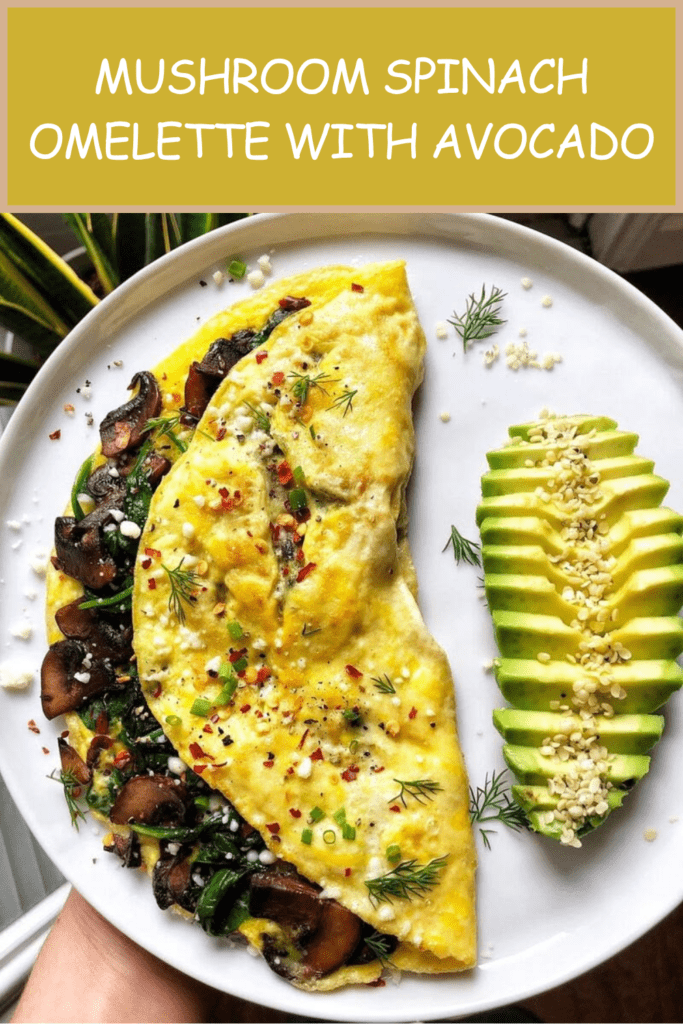 Mushroom spinach omelette served with sliced avocado, crumbled feta cheese, fresh herbs, sesame seeds, black pepper, and a small squeeze of lemon.