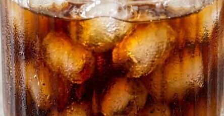 A ribbed glass tumbler filled with bullet-shaped ice cubes and freshly poured iced espresso coffee. The dark coffee cascades over the ice, creating beautiful swirling patterns in a clear aesthetic glass, served as a refreshing homemade cold coffee beverage.