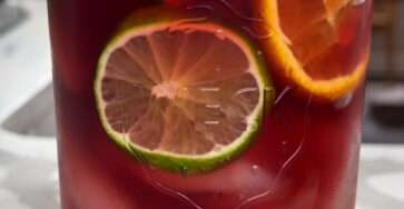 Refreshing berry citrus iced drink served with orange, lemon, lime slices, fresh berries, mint leaves, ice cubes, and sparkling water.