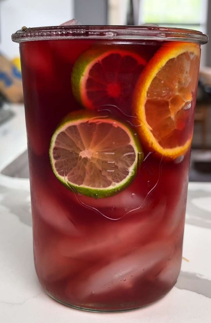 Refreshing berry citrus iced drink served with orange, lemon, lime slices, fresh berries, mint leaves, ice cubes, and sparkling water.