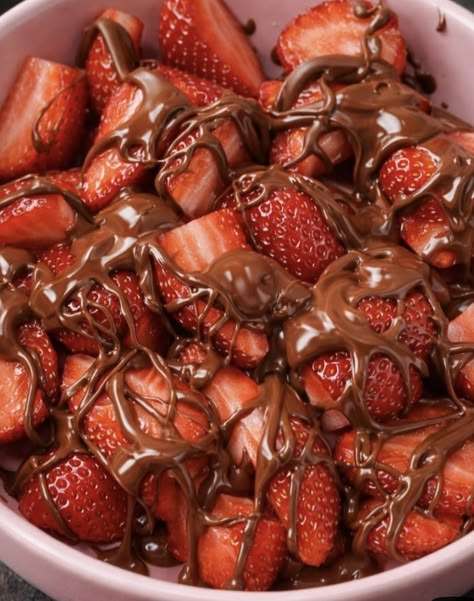 A white ceramic bowl filled with fresh red strawberry halves heavily drizzled with shiny melted dark chocolate against a clean white background.