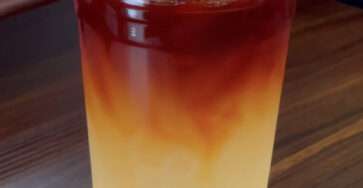 Iced lemon tea lemonade served in tall glasses with fresh lemon slices, orange slices, ice cubes, black tea layer, and mint leaves.