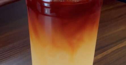 Iced lemon tea lemonade served in tall glasses with fresh lemon slices, orange slices, ice cubes, black tea layer, and mint leaves.